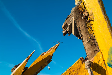 Detail of a boat wreck. Yellow painted, broken wood, nails and rope. Blue sky with trail and seagulls.の写真素材