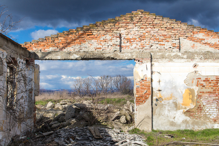 Triangle with visible bricks of the frontage of an abandoned house without a roof. Dirt everywhere in the former room. Visible nature and cloudy sky.の写真素材