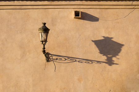 Old lantern on a dark yellow wall in the medina of Marrakesh. Long shadow during the golden hour.の写真素材
