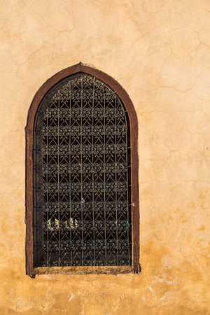 Traditional arabian window with an arch and ornamental lattice. Light orange wall, during golden hour. Medina in Marrakesh, Morocco.の写真素材