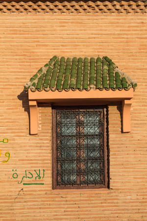 Closed window with an ornamental lattice and with a small roof with green tiles. Wall made of small bricks.の写真素材