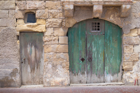 Street of an old fisher village at the island Malta, Marsaxlokk. Old green big gate with an arch and small traditional. Building made of stones.の写真素材