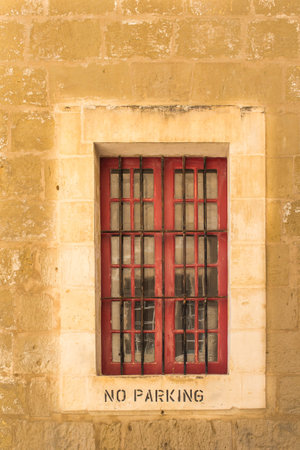 Window of a stone house with a lighter frame and a grid. No parking instruction on the frame. Former capital Mdina at the mediterranean island Malta.の写真素材