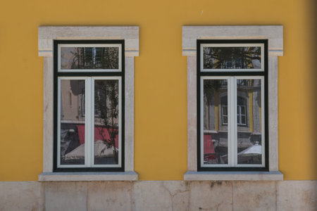 Two closed windows with a stone frame, reflecting the city. Bright yellow facade. Lisbon, Portugal.