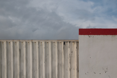 Iron structured fence and another made of concrete. Red line on the top. Cloudy stormy sky.の写真素材