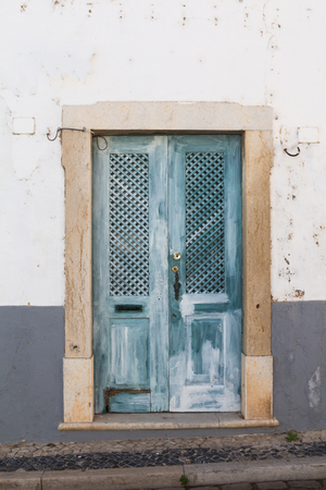 Blue wooden textured gate in a frame made of stone. White wall of the house. Street in Faro, Portugal.の写真素材