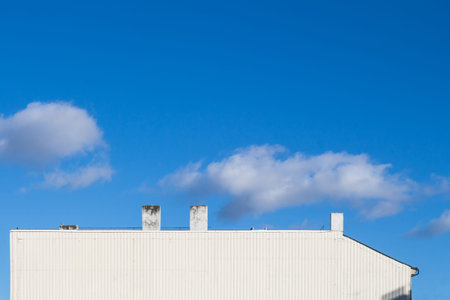 Structured white side of a house. Several chimneys. Bright blue sky with several clouds.