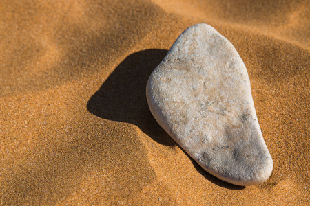 Light color of a stone in the sand of a beach. Long shadow when the sun gets down, giving to the sand a golden color.の写真素材