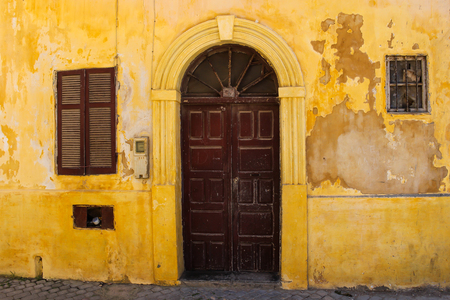 Yellow old facade of a house with wooden brown gate with an arch. Window with a shutter. Street in former portuguese fortress in El Jadida, Morocco.の写真素材