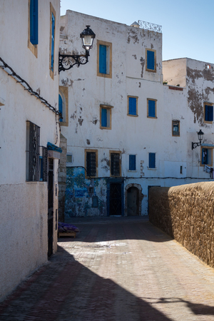 White walls of the traditional houses with small and blue shutters of the windows. Early morning street. Safi, Morocco.の写真素材
