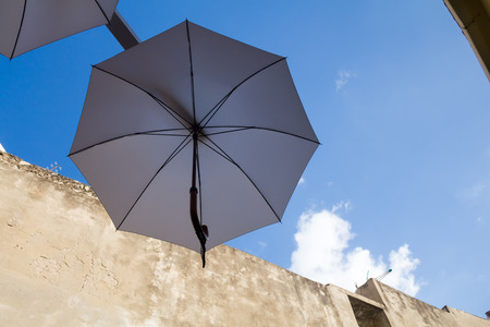 Detail of a traditional umbrella of a neutral grey color, hanging in a street to give shadow to the people. Wall of a old house in the background. Blue sky with small clouds. Rethymno, Crete, Greece.の写真素材