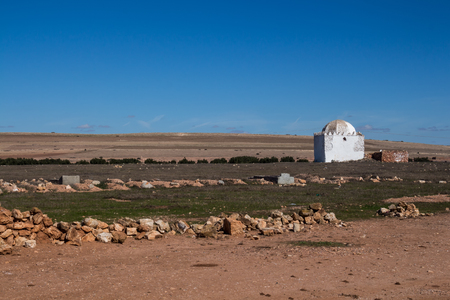 Dry autumn country with its fields and meadows. White building of a chapel / mosque of a cemetery.  Horizon in the background. Bright blue sky. Morocco.の写真素材