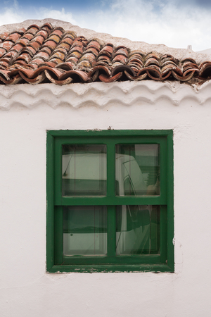 Characteristic green color of the details of the houses. White facade of a house with a window. Line of a roof and a cloudy sky. Historical village Arico Nuevo, Tenerife, Canary Islands, Spain.の写真素材