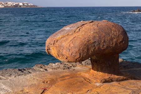Heavy and big, very rusted moor to fix the boat in the port. Atlantic ocean and a line of a blue sky in the background. Punta de Abona, Tenerife, Canary Islands, Spain.の写真素材