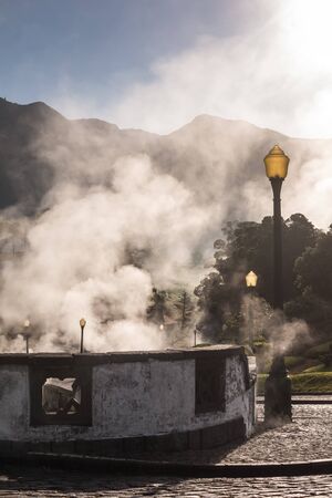 Sunny morning in a small city in a valley, with many natural hot springs, creating a steam, highlighted by the sunshine. Typical paved road and pavement. Furnas, Sao Miguel, Azores Islands, Portugal.の写真素材