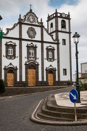 Square with typical tiles with San Jorge church. White facade and dark brown details. Cloudy sky. Nordeste, Sao Miguel, Azores Islands, Portugal.の写真素材