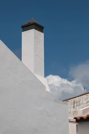 View on a side of a house with white facade and a chimney. Big white cloud in the background. Blue sky. Povoacao, Sao Miguel, Azores Islands, Portugal.の写真素材