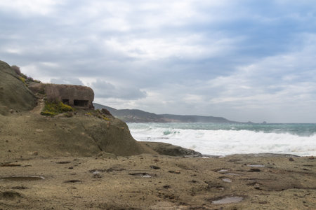 Rocky coast of the Mediterranean sea with and abandoned shelter from World War the Second. Intense rainy clouds on the spring sky. Bosa Marina, Sardinia, Italy.の写真素材