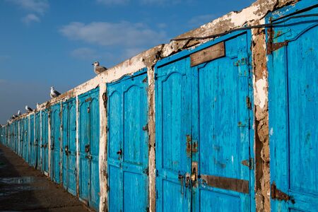 Bright blue weathered wooden doors, lining the street in an old fishing port. Essaouira, Morocco.の写真素材