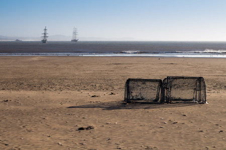 Sandy empty beach, with a pile of football goals, ready for the people to play. Early evening of the...