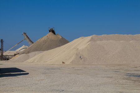 Hills of gravel at a minining plant. Dog at a bottom of the pile. Parts of machinery. Bright blue sky. Puste Ulany, Slovakiaの写真素材