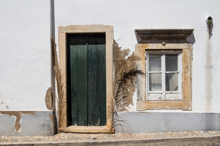White color of the facade of a house. Stone frames of the door and window. Dark green wooden door....