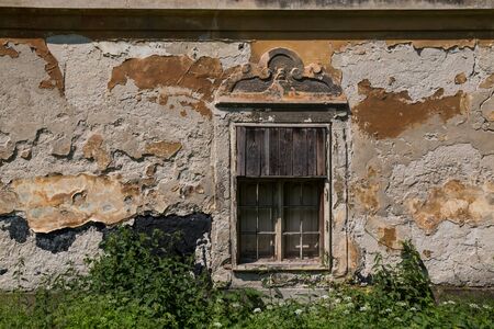 Weathered and peeled off facade of an abandoned manor house. Window partly covered by wooden laths. Jablonica, Slovakia.の写真素材