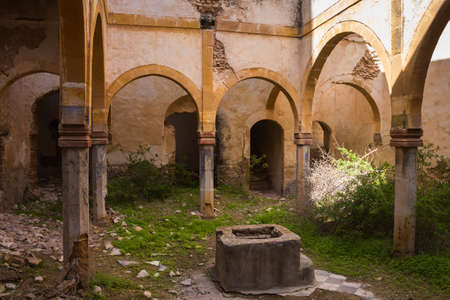 One of many yards in an abandoned house. Arcade with arcs on a columns. Base of a former fountain. Grass and plants. Dar Caid Hadji (used also Hajji), Morocco.のeditorial素材