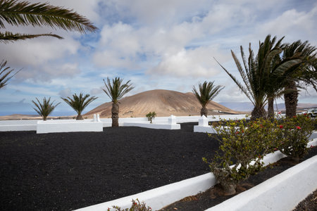 White details of the architecture, surrounding little church. View on the nature around, with a dark lava soil and a hill in the background. Cloudy sky in the late winter. La Vegueta, Lanzarote.の写真素材