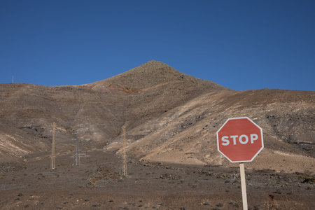 Volcanic mountains with a lot of stones and rocks on the ground. Blue sky with white clouds. Stop traffic sign on a crossroad. Lanzarote, Canary Islands, Spain.の写真素材
