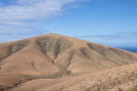 Shapes and lines of the mountains of the volcanic origin. Light brown color of the soil. Sky with clouds in the winter. Mirador Astronomico (Astronimical Viewpoint), Fuerteventura, Canary Islandsの写真素材