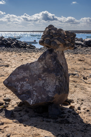 Shiny water of the Atlantic ocean in a bay, during a sunny winter day. Unique rock displayed as a statue. Blue sky with white clouds. Playa del Jablito, Fuerteventura, Canary Islands.の写真素材