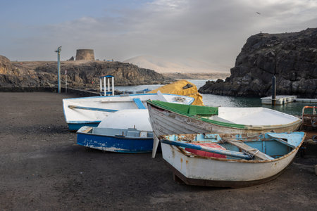 Fishing boats in the harbor out of water. Bay of Atlantic ocean, lined by rocks. Historical tower on...