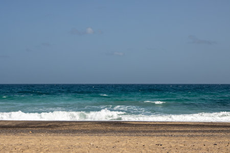 Atlantic ocean with small waves. Golden color of the sand. Blue sky on a horizon. Playa Blanca, Fuerteventura, Spain.の写真素材