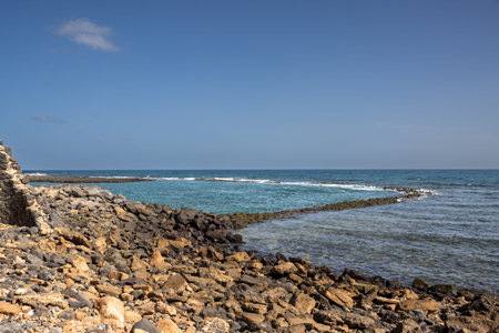 Calm water of Atlantic ocean. Many rocks and stones at the coast. Blue sky on a horizon. Hornos de...