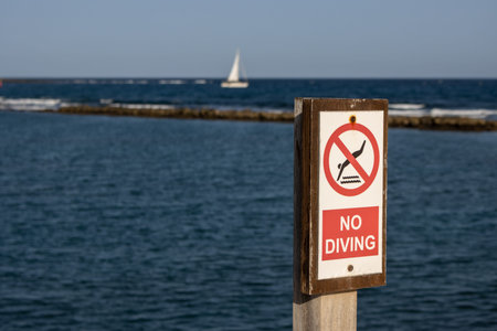 No diving advice on a wooden board. Atlantic ocean and a sailing boat in the blurry background. Blue...