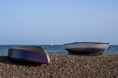 Couple of fishing boat on the pebble beach. Calm water of Atlantic ocean and blue sky. Sailing boat on the horizon. Pozo Negro, Fuerteventura, Canary Islands, Spain.の写真素材