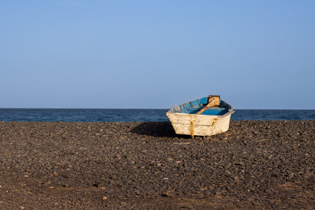 Wooden fishing boat on a pebble beach. Calm Atlantic ocean and a blue sky with a touch of golden hour. Pozo Negro, Fuerteventura, Canary Islands, Spain.の写真素材