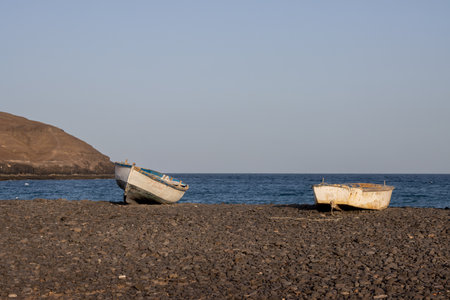 Couple of fishing boat on the pebble beach. Calm water of Atlantic ocean and blue sky. Sailing boat on the horizon. Pozo Negro, Fuerteventura, Canary Islands, Spain.の写真素材