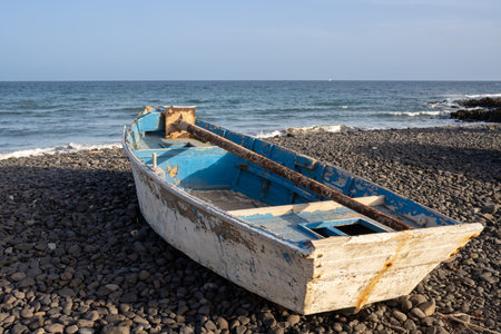 Wooden fishing boat on a pebble beach. Calm Atlantic ocean and a blue sky with a touch of golden hour. Pozo Negro, Fuerteventura, Canary Islands, Spain.の写真素材