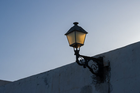 Classical shape of a metal street lantern on the edge of the wall of a house. Colored by a light of...