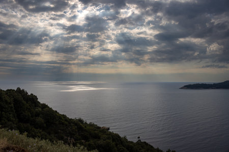 Diagonal line of a nature on a hill and view on the Thracian sea, enlightened by rays of sunshine cross an intense clouds in the late summer. South of Thassos (Thasos), Greece.の写真素材