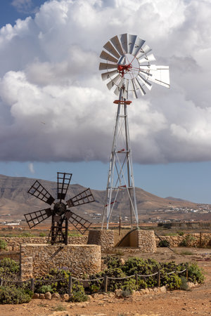 Decorative small windmill in a park. Wind generator in the background. Blue sky with intense white clouds. Llanos de la Concepcion, Fuerteventura, Canary Islands, Spain.の写真素材