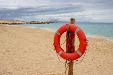 Curve of the sandy beach of Atlantic ocean. Empty in the winter season. Cloudy sky. Reflection red lifebuoy in the foreground. Dunas de Corralejo, Fuerteventura, Canary Islands, Spain.の写真素材