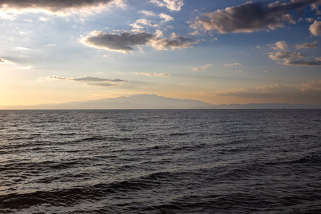Calm  water of Aegean sea (Mediterranean) during Golden hour. Mountains of the continental Greece on a horizon. Sky with light clouds in the late summer. Thassos (Tassos) west, Greece.の写真素材