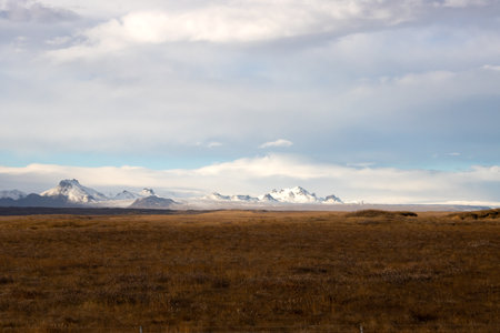 Country with meadows, fields or pastures, dry in the autumn. Mountains with snow on the horizon. Blue sky with white clouds. Gullfoss area, south-middle part of Iceland.の写真素材