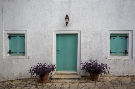 White facade of a house with bright green closed wooden door and window shutters. Lantern above the...