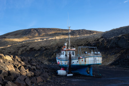 Old abandoned rusted fishing boat on the volcanic soil. Mountains in the background.. Blue sky. Bakkagerdi, Iceland.の写真素材