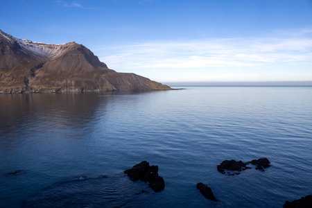 Autumn nature on the North-East part of the island. Majestic mountains around the fjord, covered by lichen and moss. Calm water of Atlantic ocean. Blue sky with light clouds. Hafnarholmi, Iceland.の写真素材