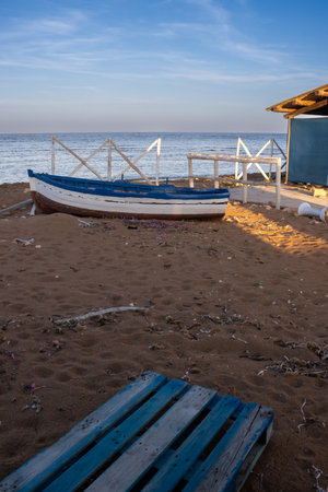Calm water of the Mediterranean sea. White wooden fence, small beach house and a wooden boat in the sand, together with blue palette. piaggia Sibilliana, Marsala, West Sicily, Italy.の写真素材